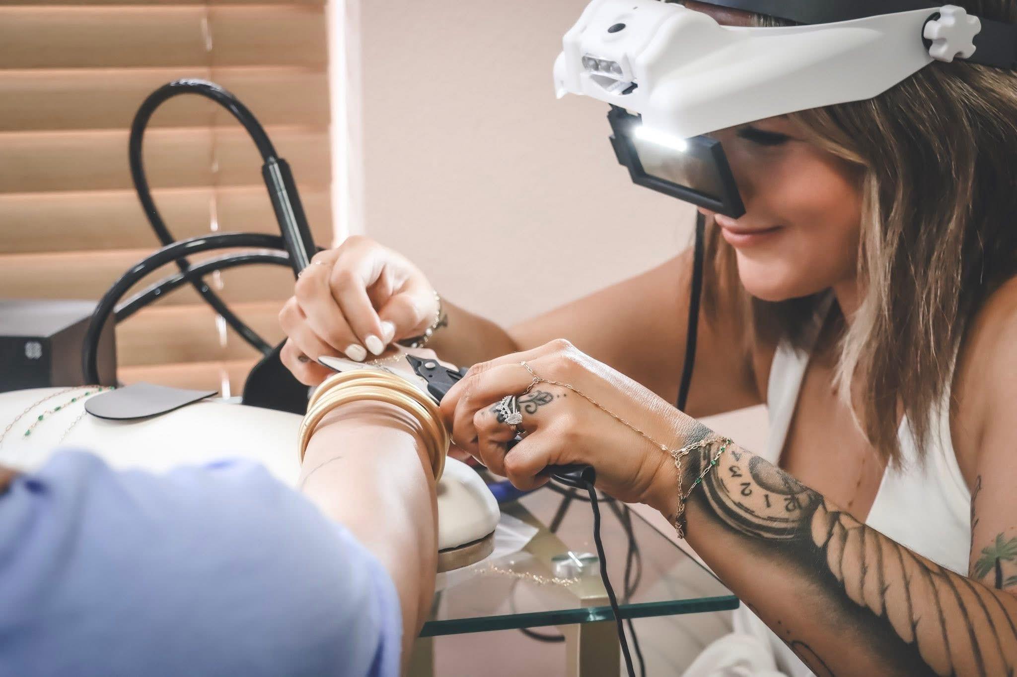 Person getting a permanent Jewelry bracelet by a woman wearing a permanent jewelry welding mask.